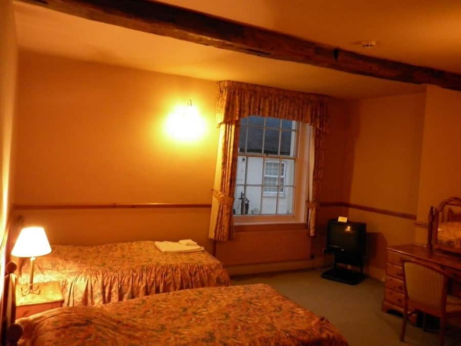 Une chambre avec deux lits, une fenêtre avec des rideaux, une lampe, un téléviseur et une chaise en bois.