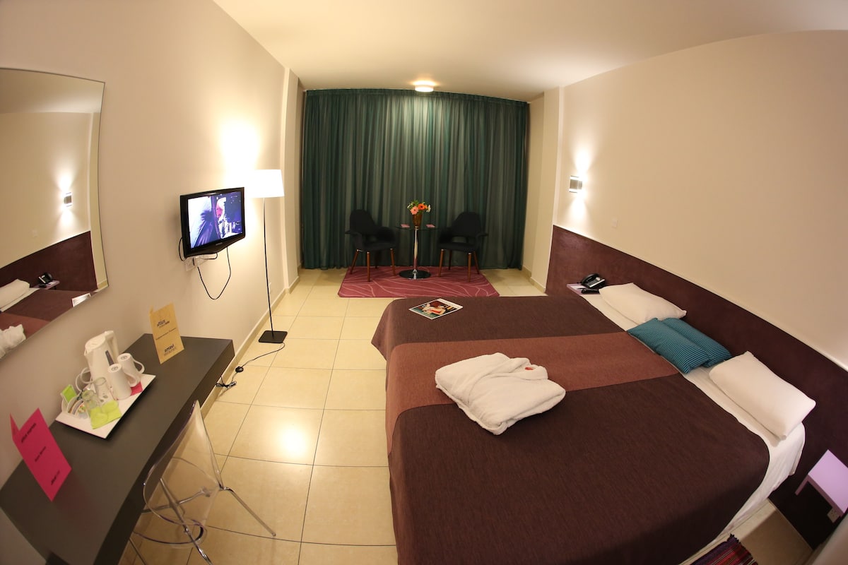 Una habitación de hotel con una cama, un escritorio con artículos de aseo, un televisor y vistas al resto de la habitación.