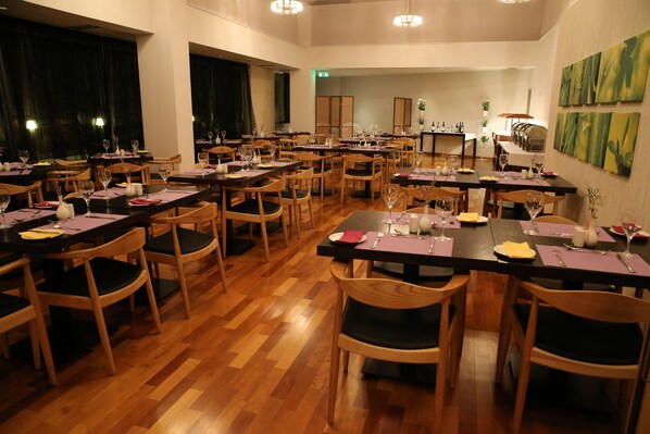 A spacious dining area with multiple tables and chairs, wooden flooring, and wall-mounted artwork.