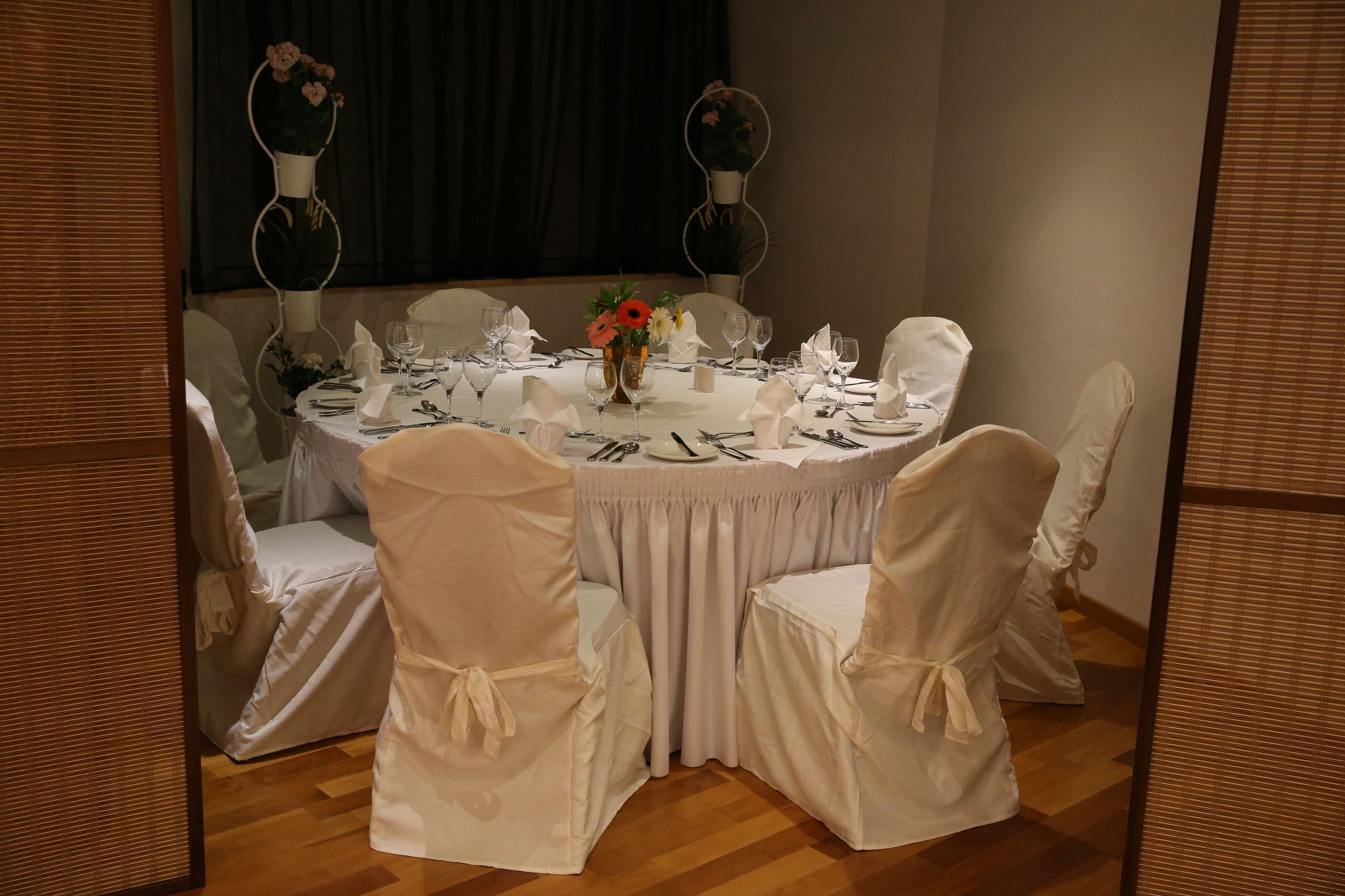 A round dining table with white tablecloth and chairs, set for a meal.