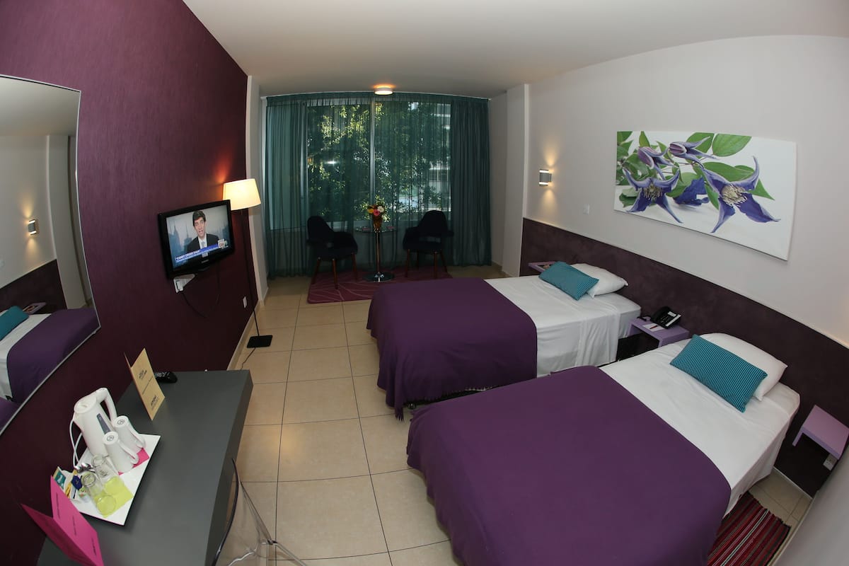 Habitación de hotel con dos camas, un televisor, un escritorio con cafetera y un cuadro en la pared.