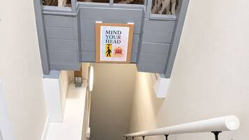 A staircase with a handrail, a 'MIND YOUR HEAD' safety sign, and a patterned carpet.