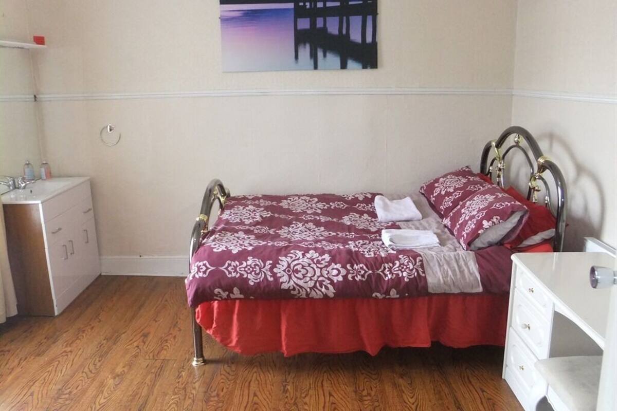 Ein Schlafzimmer mit einem Bett, einem Schminktisch, einem Nachttisch und einem Bild eines Piers an der Wand.