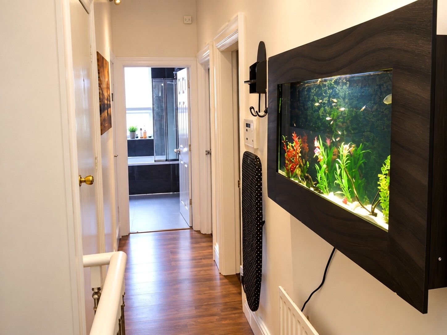 Een hal met een houten vloer, een radiator en een aan de muur bevestigd aquarium.