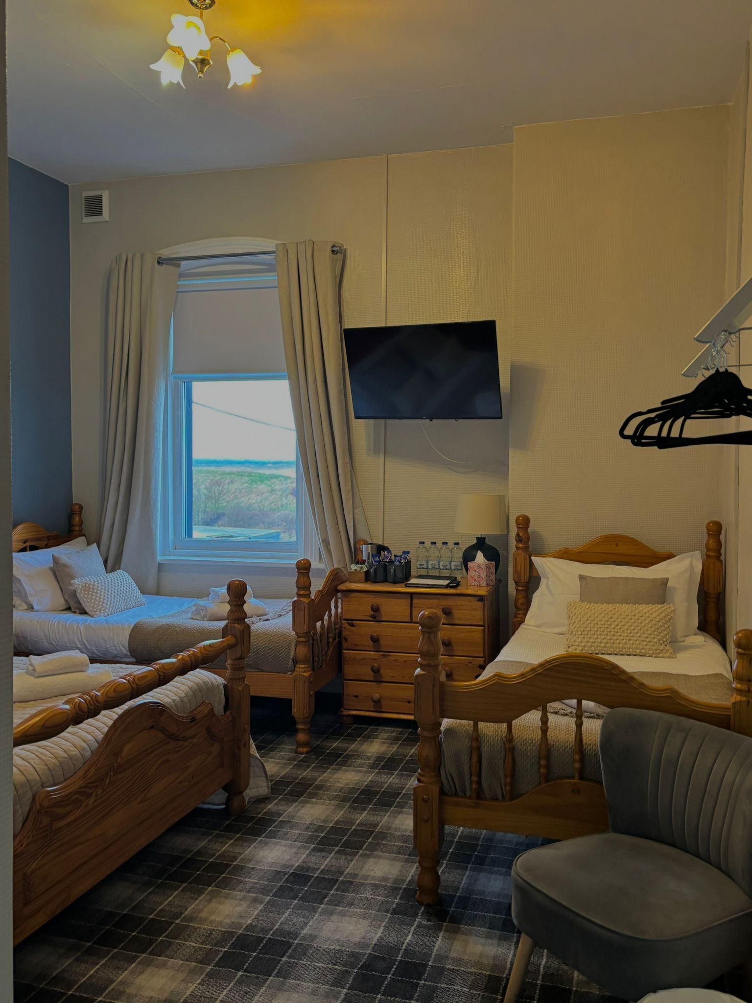 A room with two wooden beds, a TV mounted on the wall, a dresser, and a window with curtains.