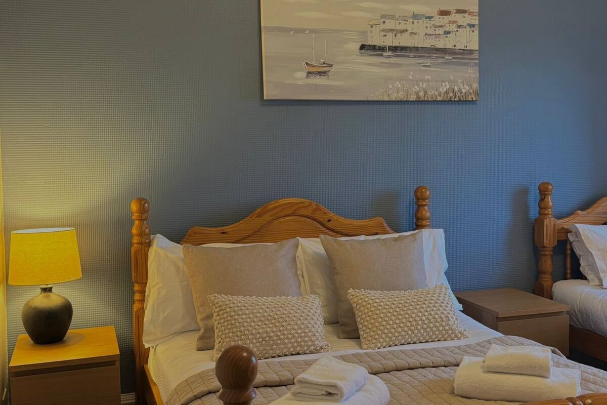 A neatly made bed with a wooden headboard, a bedside lamp, and a painting of a coastal scene on the wall.