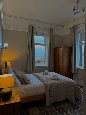 A neatly made bed with a quilt, a wooden wardrobe, and a lamp on a bedside table. - The Waterford Arms (Whitley Bay)