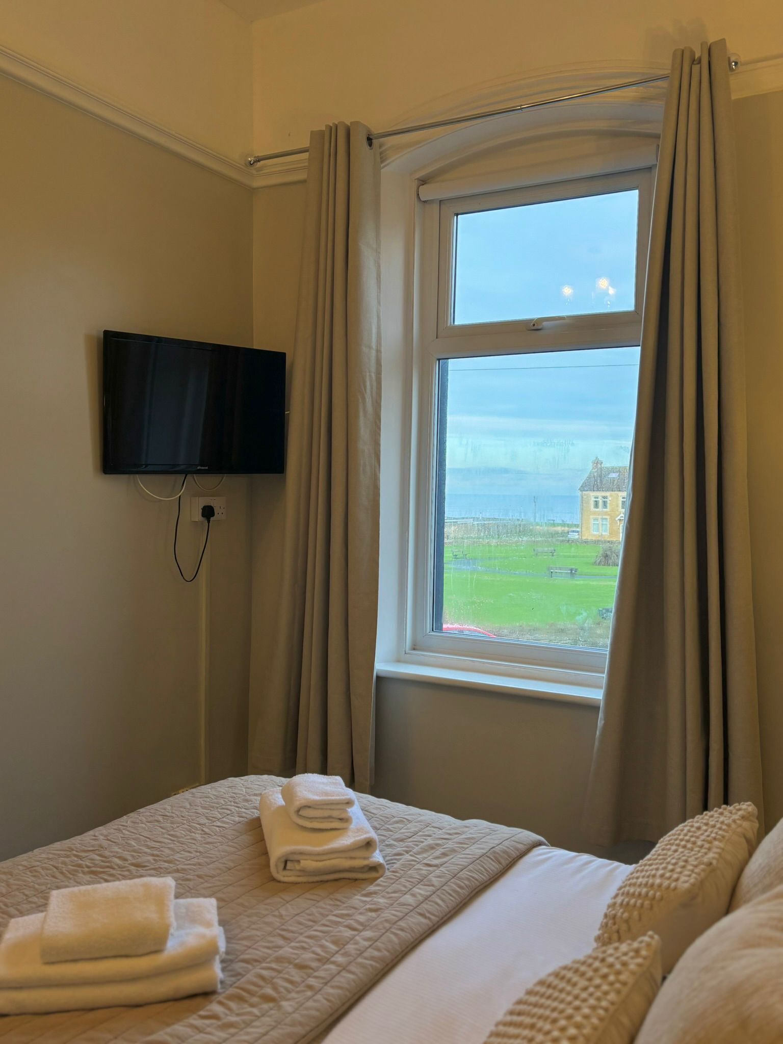 A hotel room with a bed, a TV mounted on the wall, and a window with curtains.