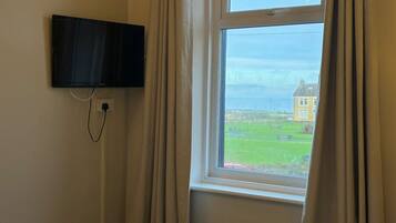 A hotel room with a bed, a TV mounted on the wall, and a window with curtains.