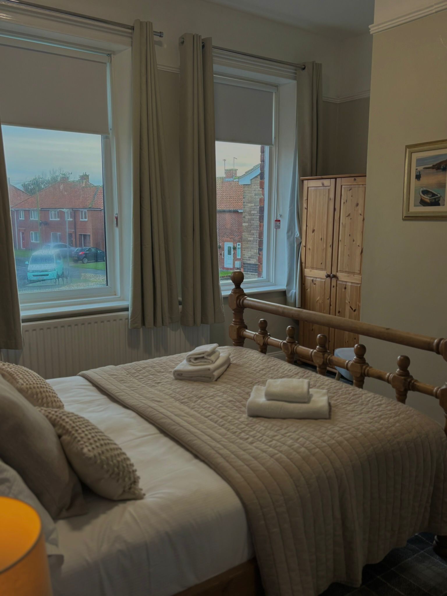 A bedroom with a bed, a window with curtains, a radiator, and a wooden wardrobe.