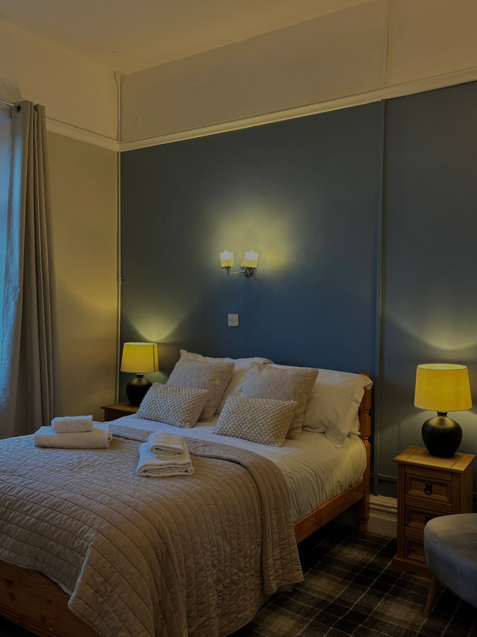A neatly made bed with a quilted cover, two bedside lamps, and a wall-mounted light fixture.