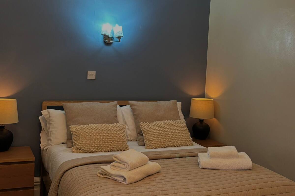 A neatly made bed with a beige quilt, two bedside lamps, and a wall-mounted light fixture.
