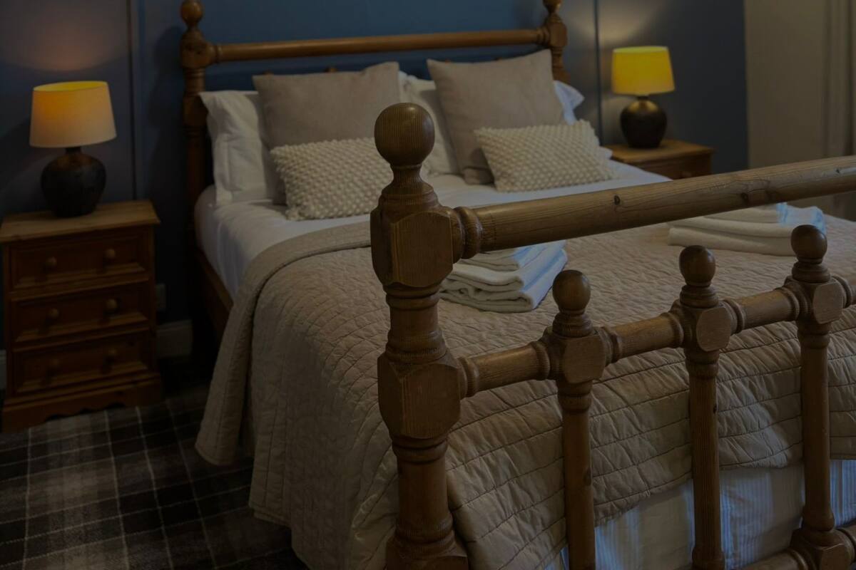 A bedroom with a wooden bed, two bedside tables with lamps, a painting on the wall, and a plaid floor.