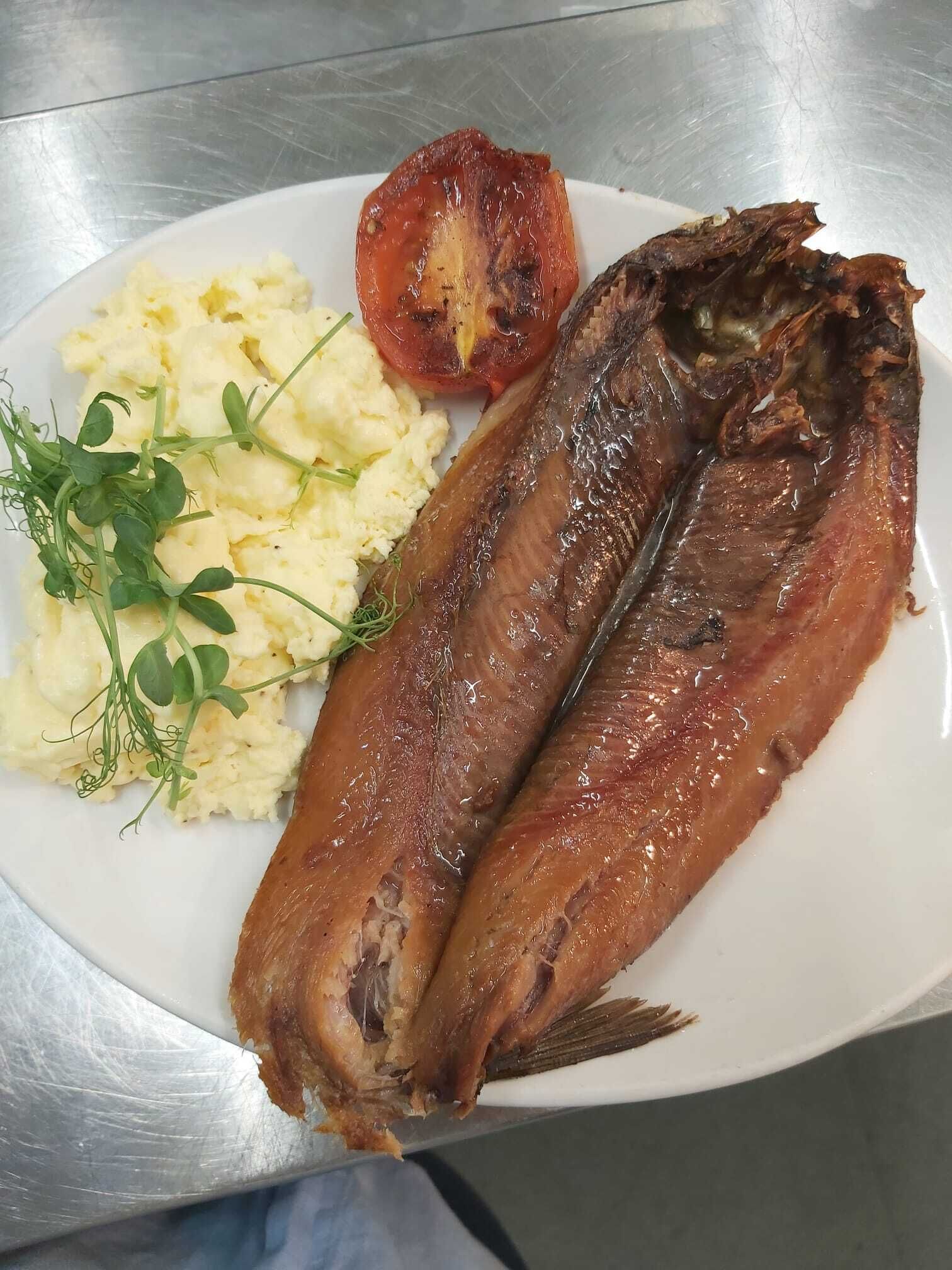 Ein Teller mit zwei gegrillten Fischen, Kartoffelpüree, einer gegrillten Tomate und etwas Salat.
