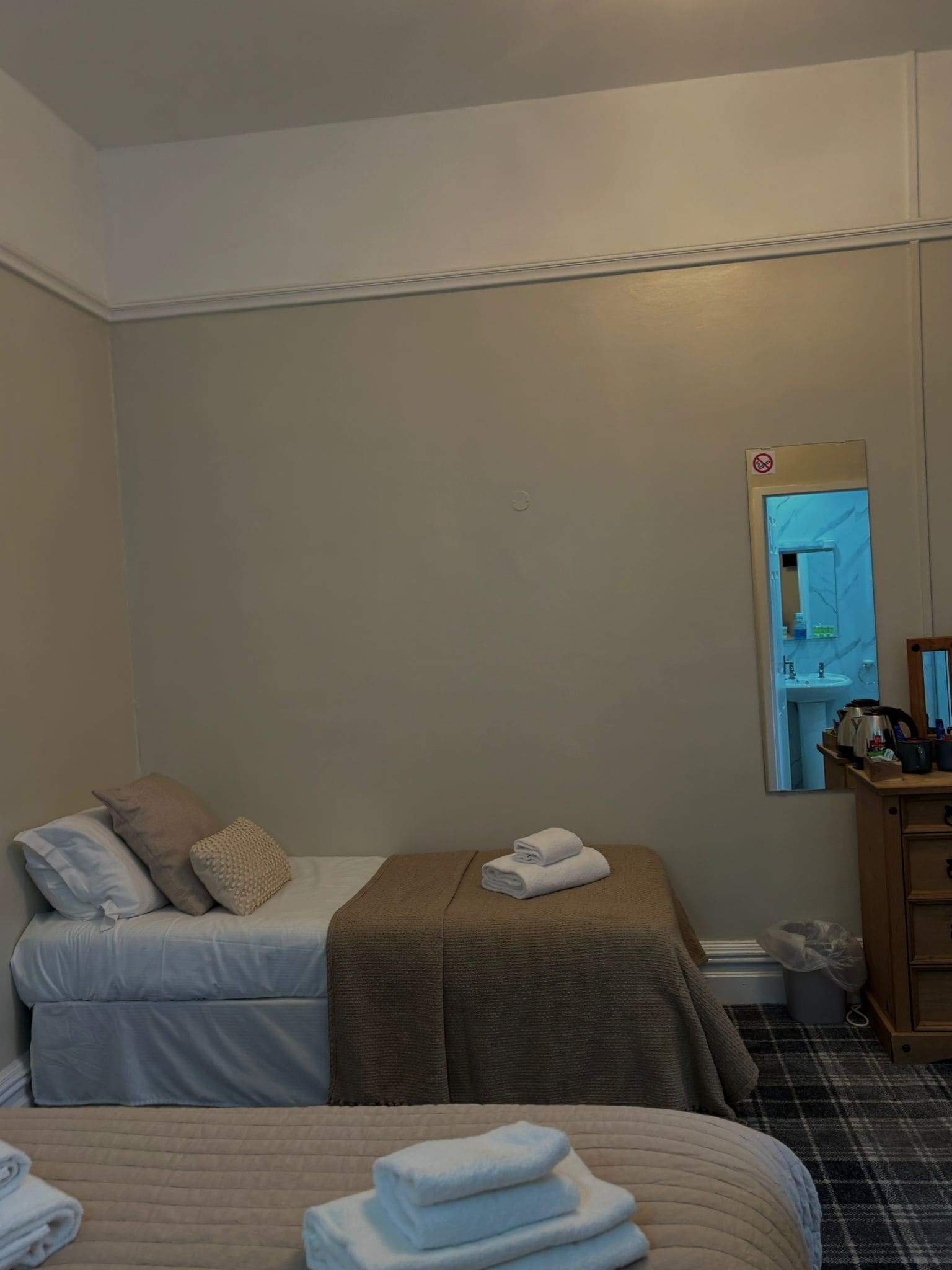 A hotel room with two beds, a small desk, a mirror, and a view of the bathroom.