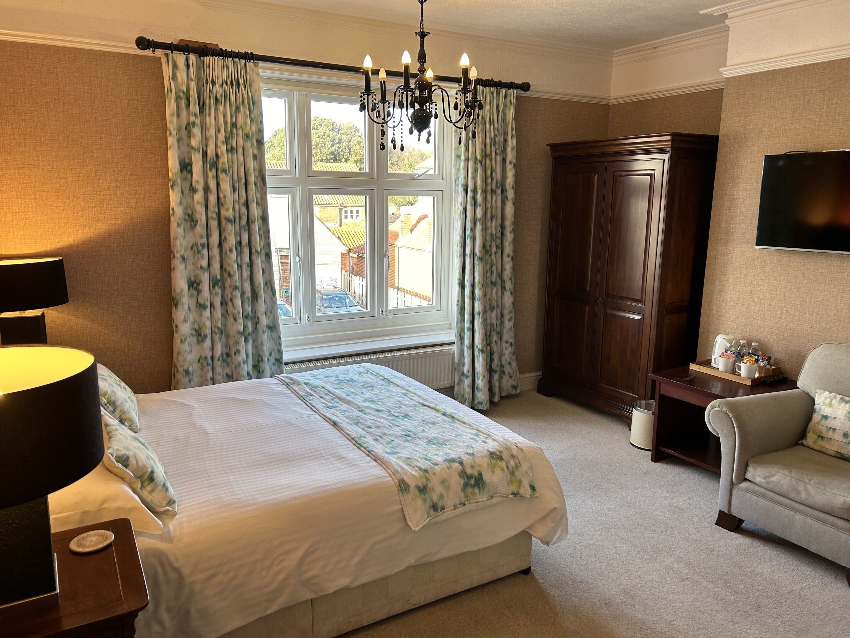A hotel room with a large bed, a wooden wardrobe, a television, and a window with curtains.