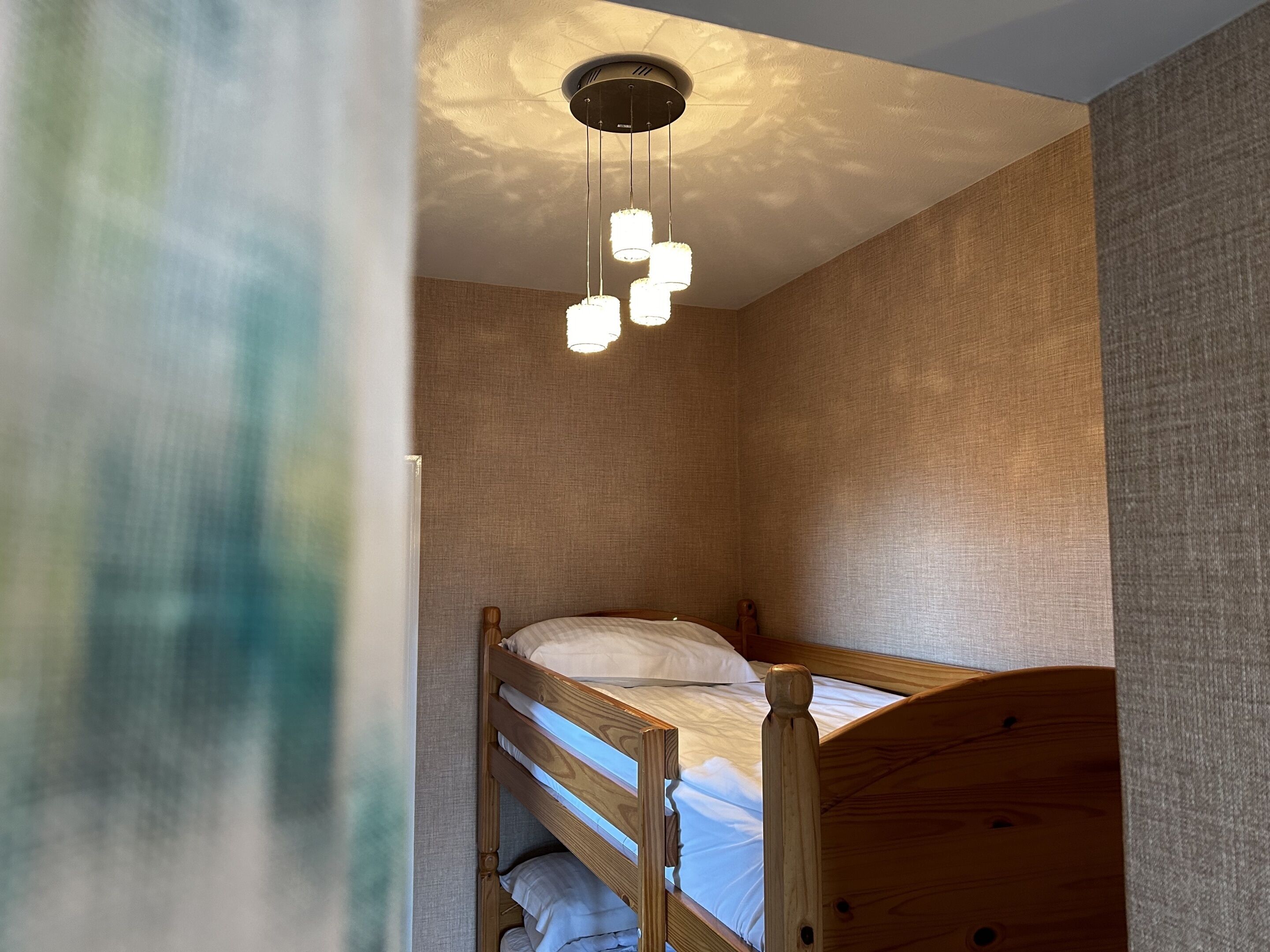 A small, cozy room with a bunk bed, a ceiling light fixture, and textured walls.