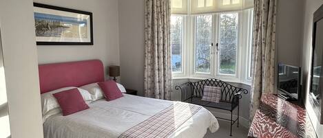 A bedroom with a bed, a desk, a chair, a window with curtains, a chandelier, and a painting on the wall.