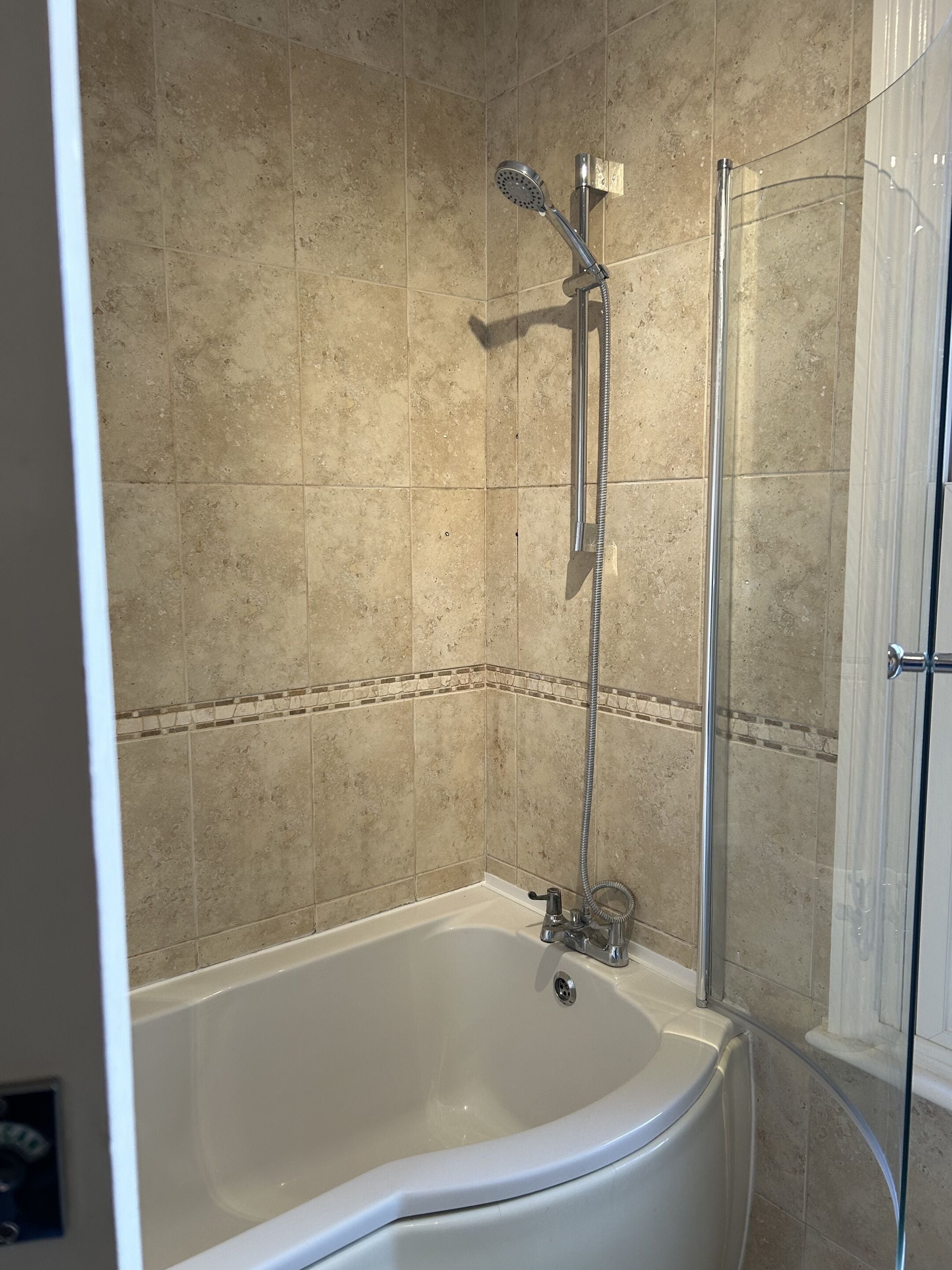 Un bagno con una vasca, una doccia con cabina in vetro e pareti rivestite di piastrelle color beige.