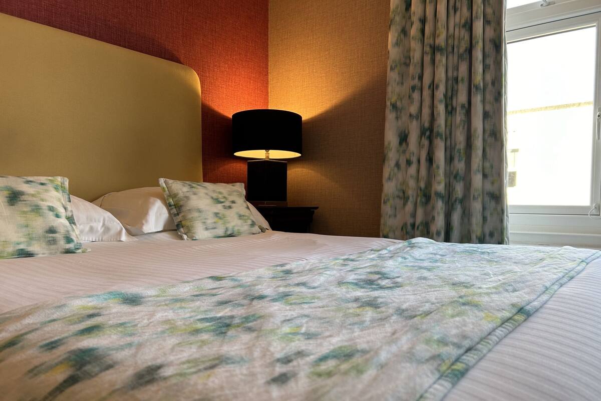 A hotel room with a bed, a nightstand with a lamp, and a window with curtains.