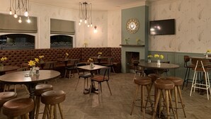 Ein Restaurant mit runden Tischen, Barhocker, einem Kamin und einem an der Wand befestigten Fernseher.