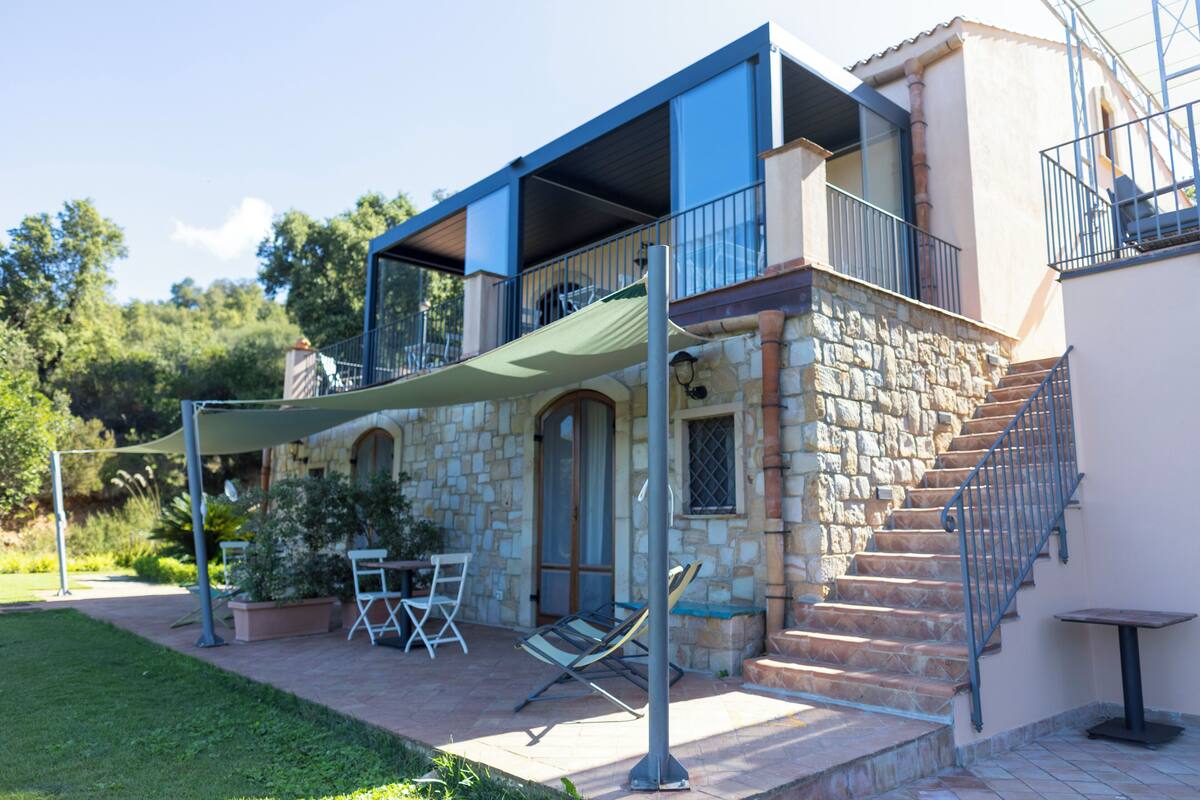 A two-story stone house with a balcony, outdoor seating, and a staircase.