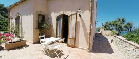 A Mediterranean-style building with a tiled patio, a table and chairs, and a potted plant.