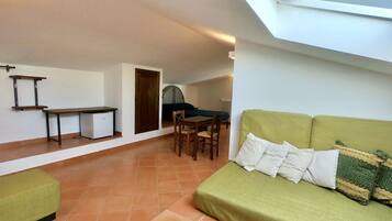 Un espacio habitable compacto con un sofá verde, una pequeña mesa de comedor y una zona de kitchenette.