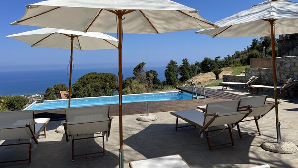 Área da piscina com espreguiçadeiras e guarda-sóis, com vista para a piscina e para a paisagem marítima.