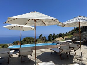 A poolside area with lounge chairs and umbrellas, overlooking a pool and a scenic view of the sea. - B&B Le Ginestre (Cefalù)