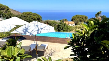 Zona de piscina con vista al mar, rodeada de vegetación y una terraza de madera.