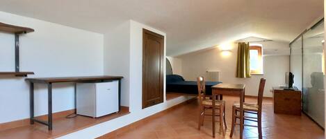A compact living space with a kitchenette, a dining area with a table and chairs, a bed, and a glass partition wall.
