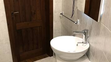 Un baño con puerta de madera, lavamanos blanco, toallero y felpudo azul.