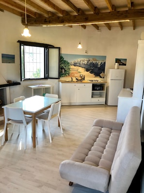 A modern kitchen with white cabinets, a dining table with chairs, a beige sofa, and wooden beams on the ceiling. - Masseria La Torre (Corigliano D'Otranto)