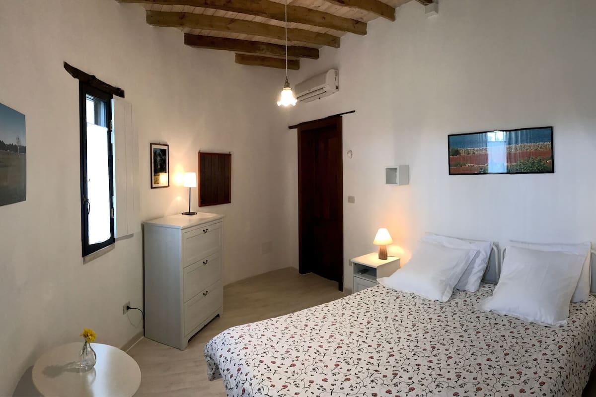 A bedroom with a bed, bedside tables, a dresser, a window, and wall-mounted artwork.