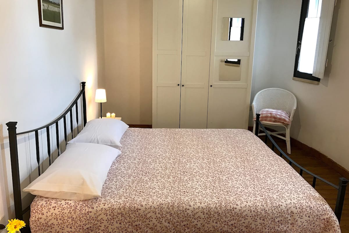 A bedroom with a bed, a chair, a wardrobe, and a window.