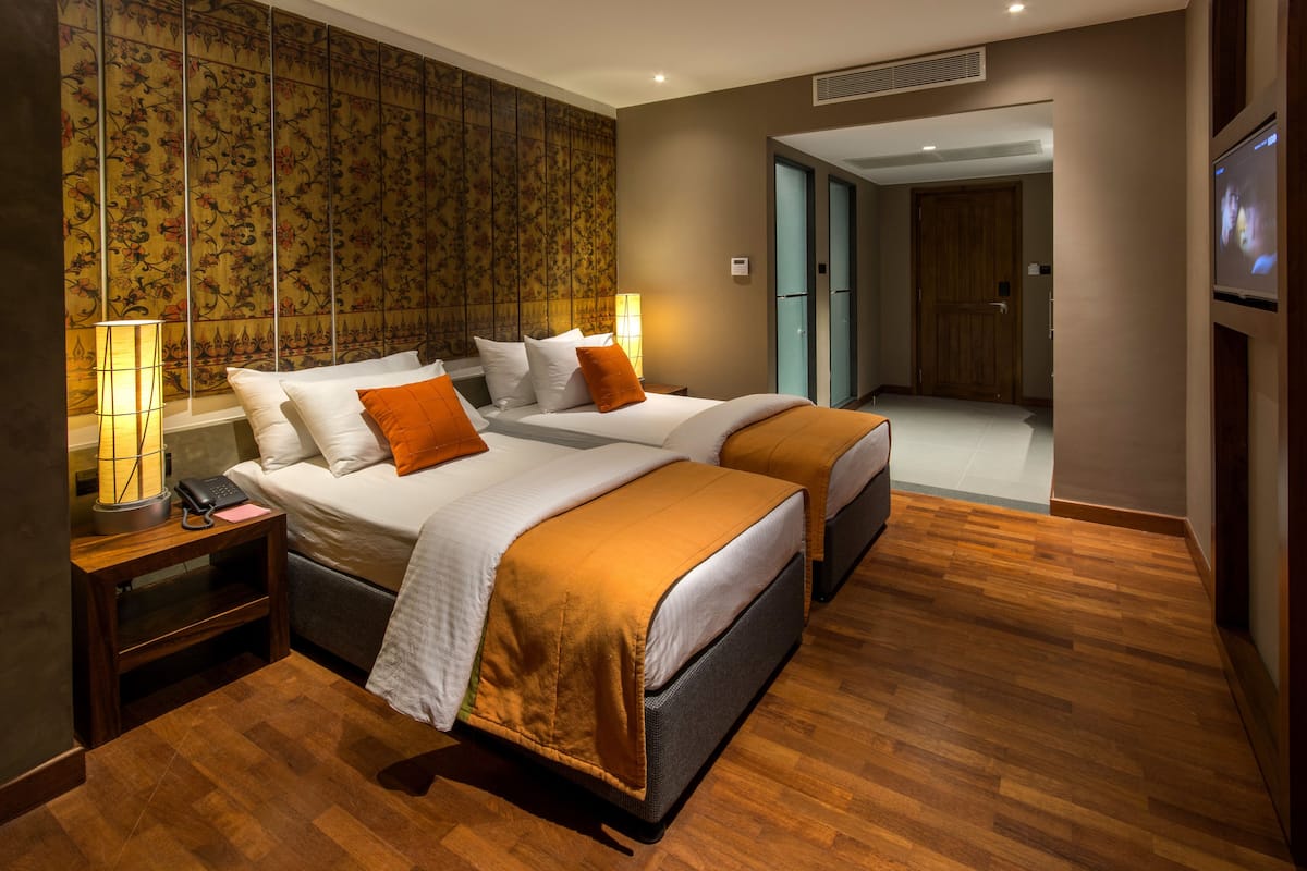 A hotel room with two beds, a wooden floor, a large mirror, and a TV on the wall.