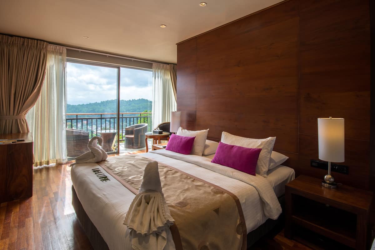 A hotel room with a large bed, a wooden headboard, a nightstand with a lamp, a chair, and a view of the outdoors.