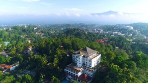 An aerial view of a hotel surrounded by lush greenery, with a mountain range in the background. - The Swiss Residence (Kandy)