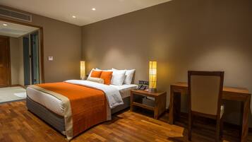 A hotel room with a bed, bedside table, chair, and a desk.
