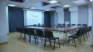 A conference room with a long table, chairs, a projector screen, and a presentation on a wall. - Gordon Hotel (Warsaw)