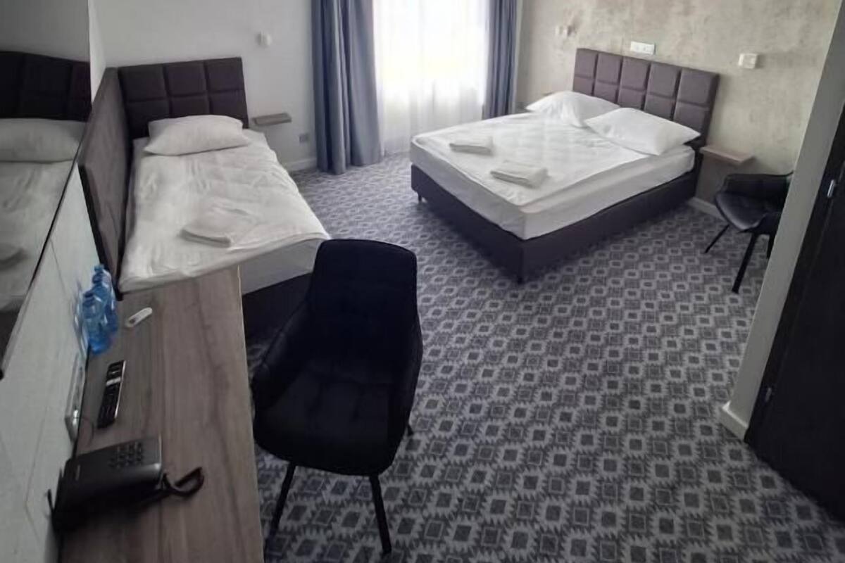 A hotel room with two beds, a desk, a chair, and a small table.