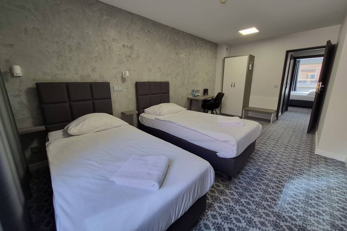 A hotel room with two beds, a desk, a chair, and a wardrobe.
