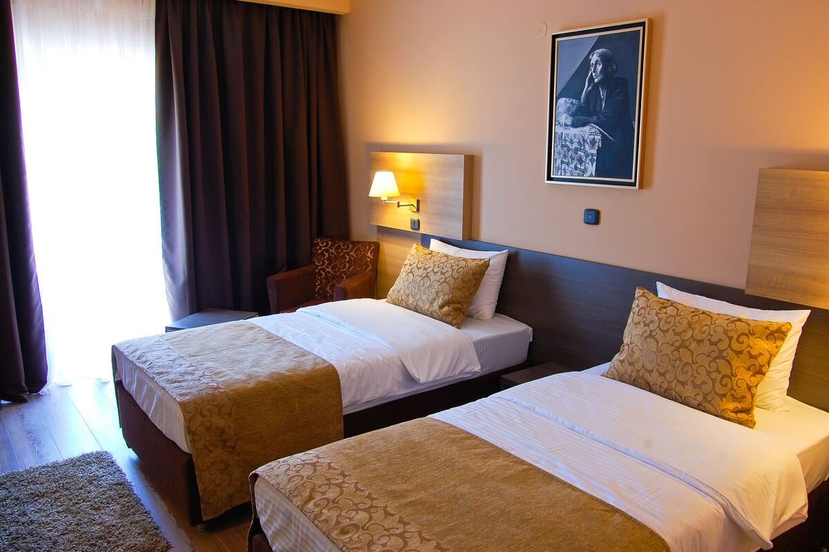 A hotel room with two beds, a nightstand, a lamp, and a framed picture on the wall.