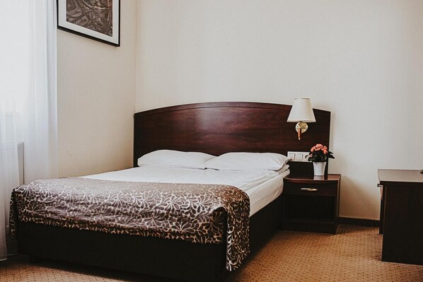 Una habitación de hotel con una cama, una mesita de noche con una lámpara y una pequeña mesa con un florero.
