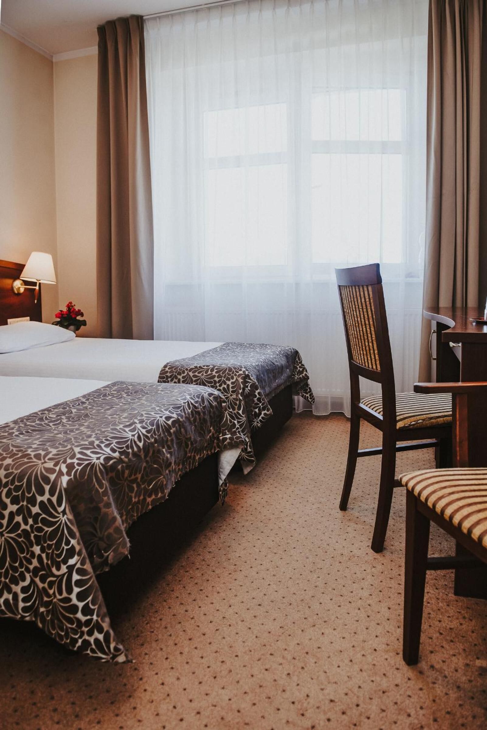 Habitación de hotel con dos camas, un escritorio, una silla y una ventana con cortinas.