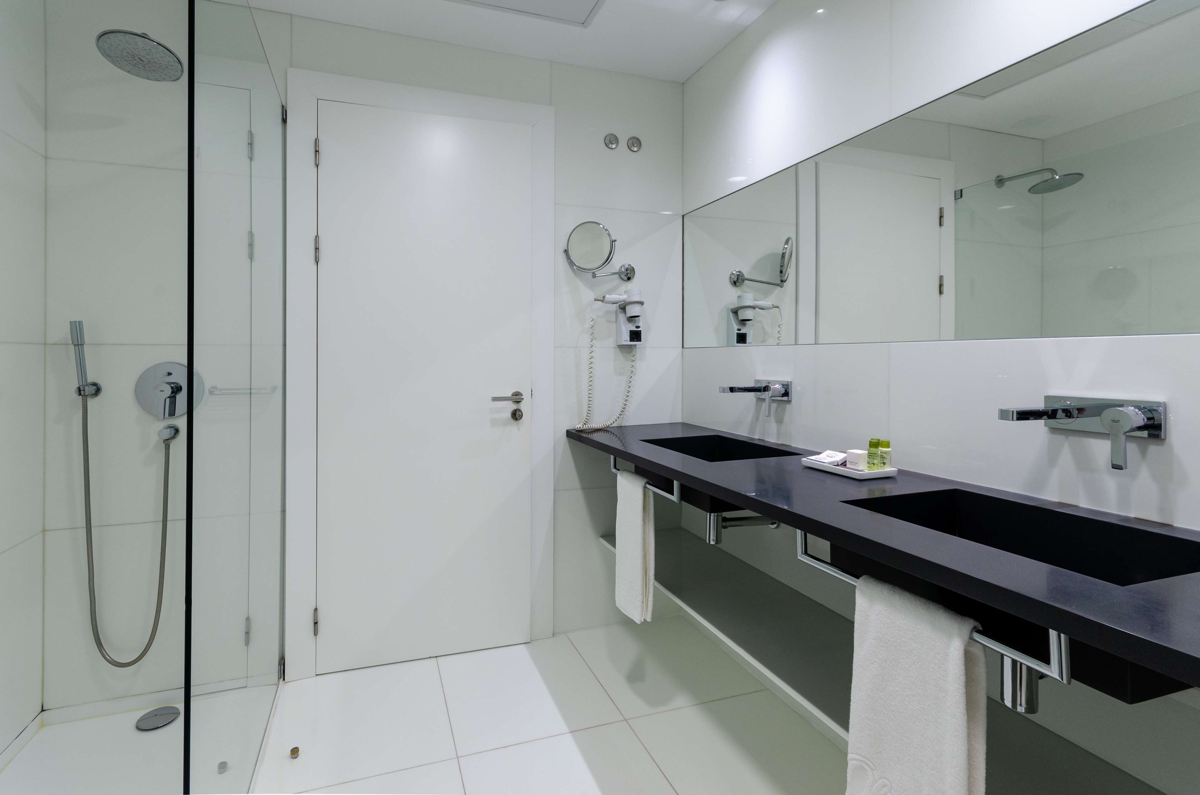 A modern bathroom with a glass-enclosed shower, two sinks, a large mirror, and a towel rack.