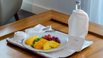 A tray with a plate of fruit, a bottle, and a card on a wooden table.
