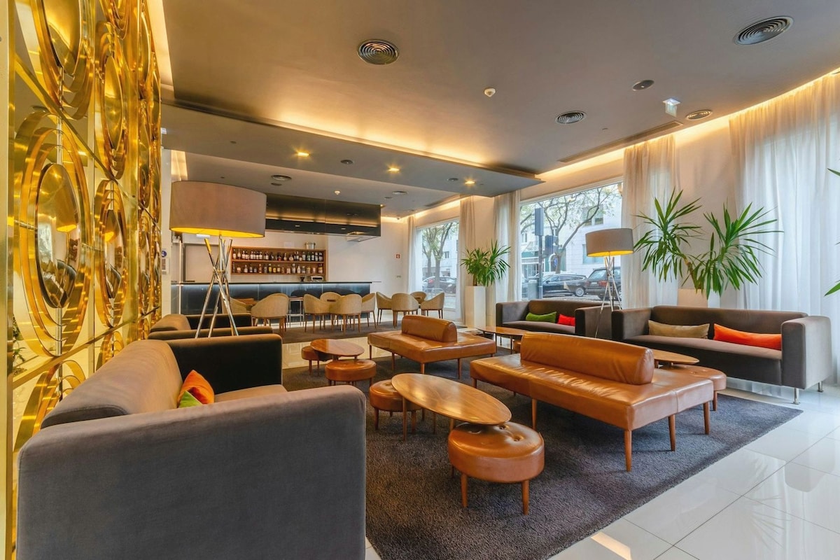 Een moderne hotelhal met leren banken, houten salontafels en een bar met flessen.