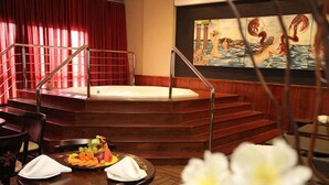 A spa area with a hot tub, wooden steps, a dining table with a fruit platter, and a painting on the wall. - Ecologic Ville Resort & Spa (Caldas Novas)